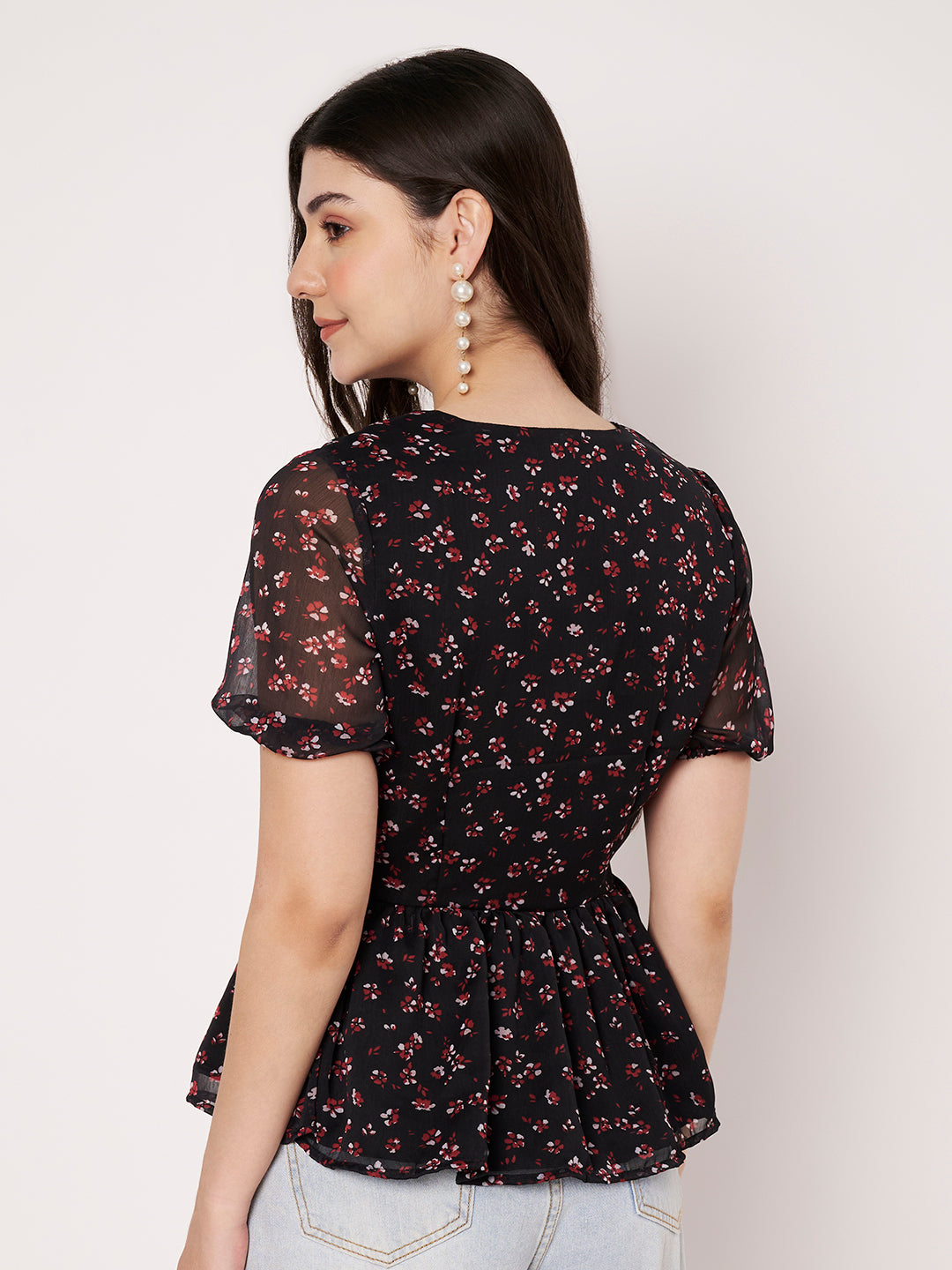 Back profile of a women's black floral print peplum top showing sleeve and waist detail.